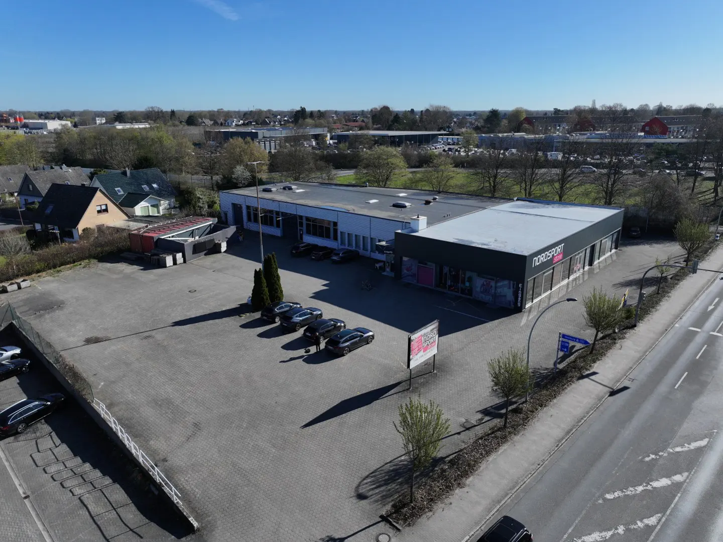 Aerial view of Nordsport store with a large parking lot, cars, and surrounding buildings under a clear blue sky.