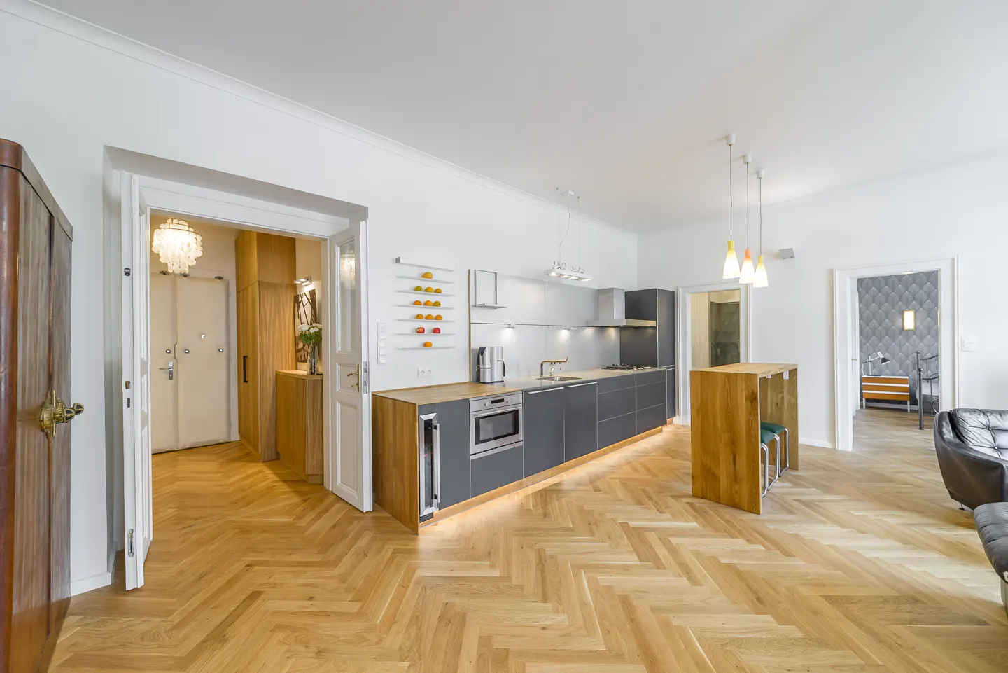Bright, modern kitchen with herringbone wood floors, gray cabinets, and white walls. Open doorways lead to other rooms.