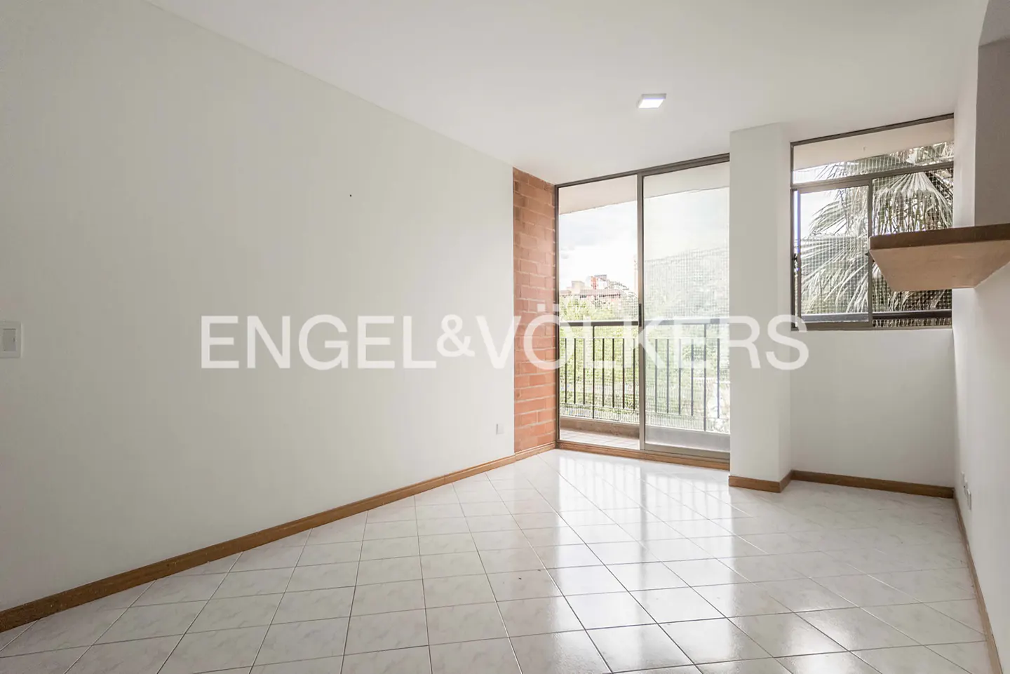 Empty room with white walls, tiled floor, brick accent wall, and sliding glass doors leading to a balcony.