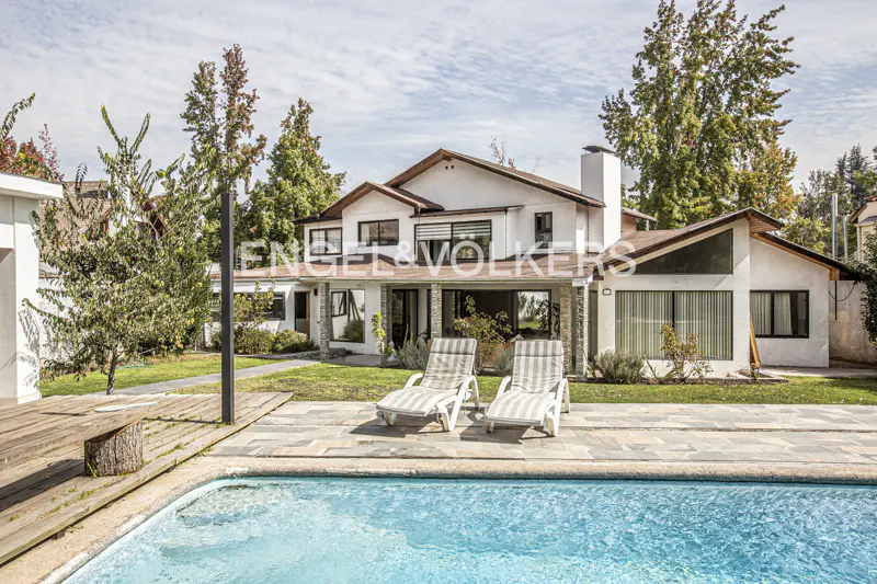 Exterior view of a two-story white house with a pool and two lounge chairs in the backyard. Trees surround the property.