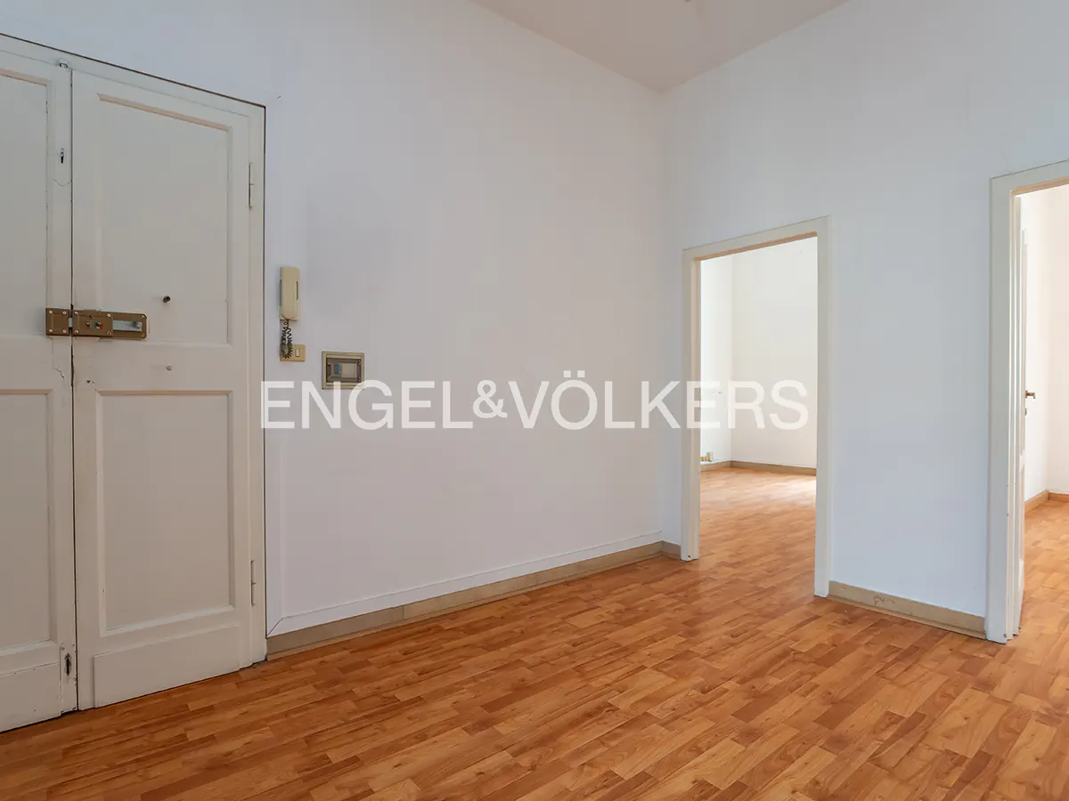 A bright room with wood floors, white walls, and two open doorways. A white door is on the left. The Engel & Völkers logo is on the wall.