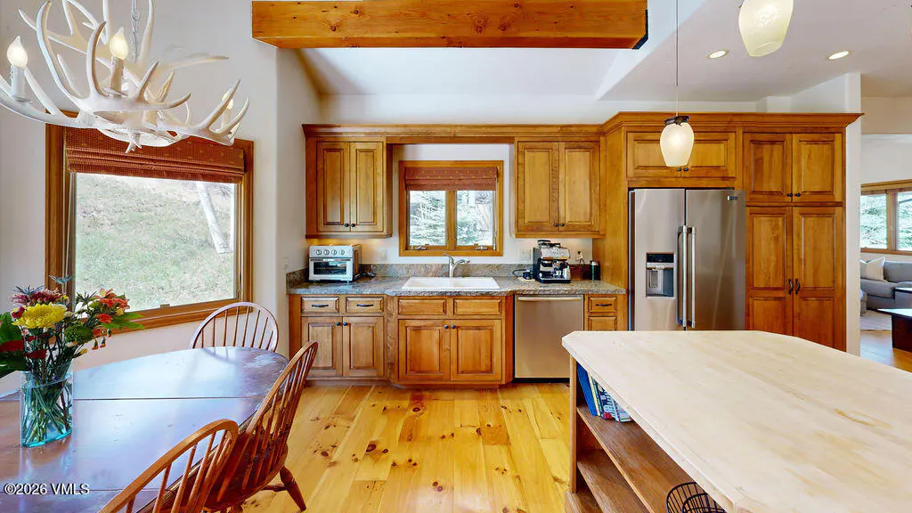 A kitchen with wood cabinets, stainless steel appliances, and a wood island. A table with flowers sits near a window. An antler chandelier hangs above.