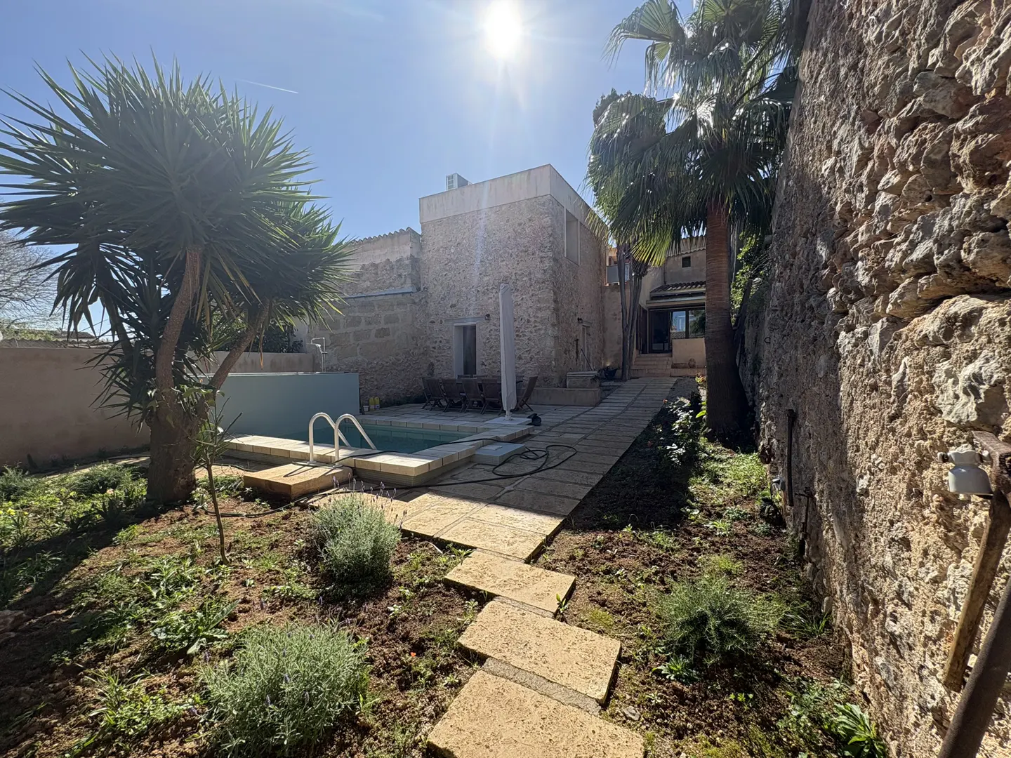 Backyard view of a stone house with a pool, palm trees, and stone pathway on a sunny day.