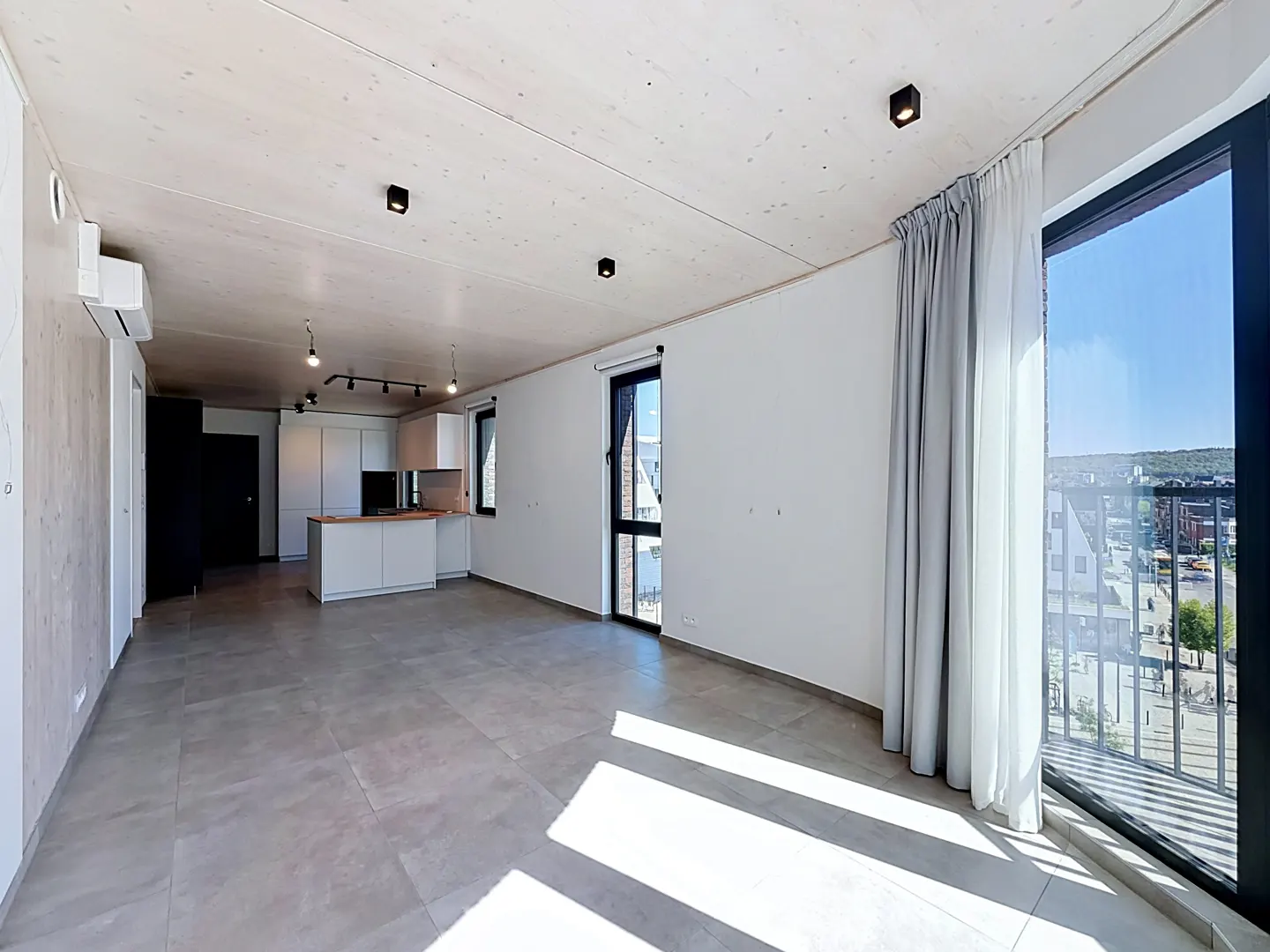 Bright, modern apartment interior with gray tile floors, white walls, and a kitchen island. Large windows offer a city view.