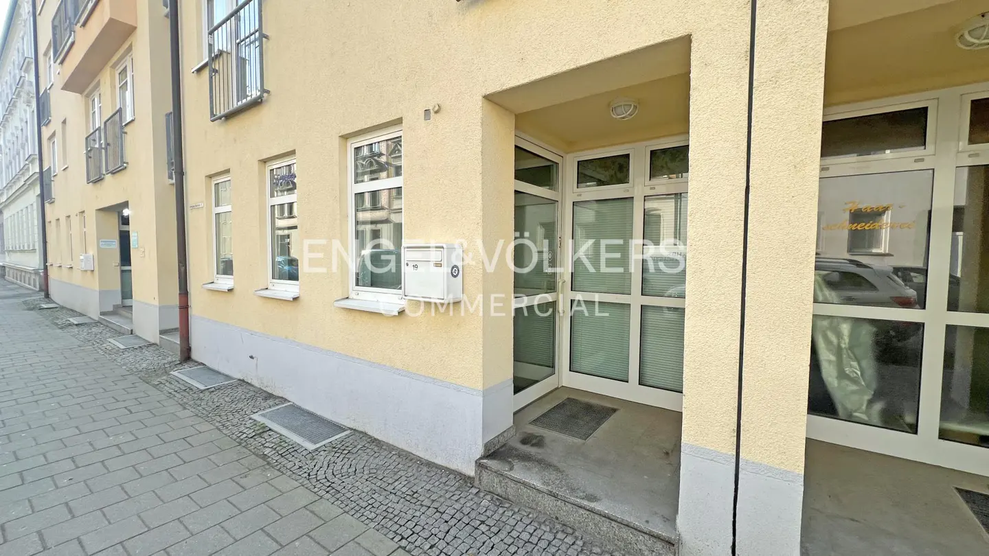 Exterior view of a yellow building with an Engel & Völkers Commercial office entrance. The door is glass with white frames.