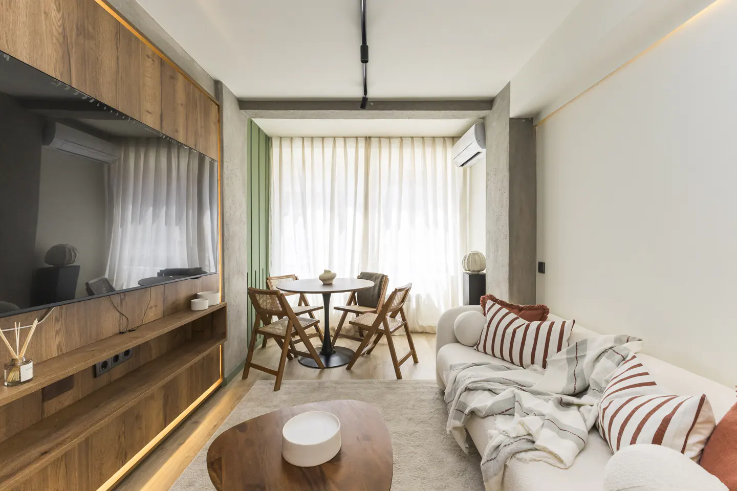 Living room with a wood entertainment center, a round table with four chairs, and a white sofa with striped pillows.