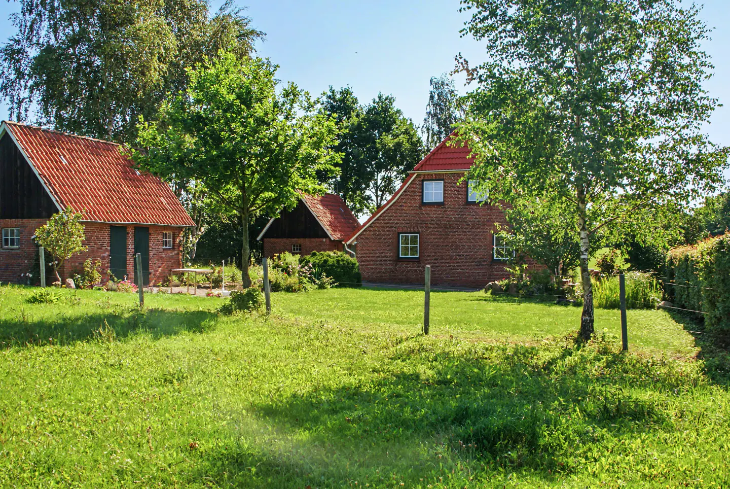 Exterior view of a red brick house with a red tile roof, surrounded by green grass and trees on a sunny day.