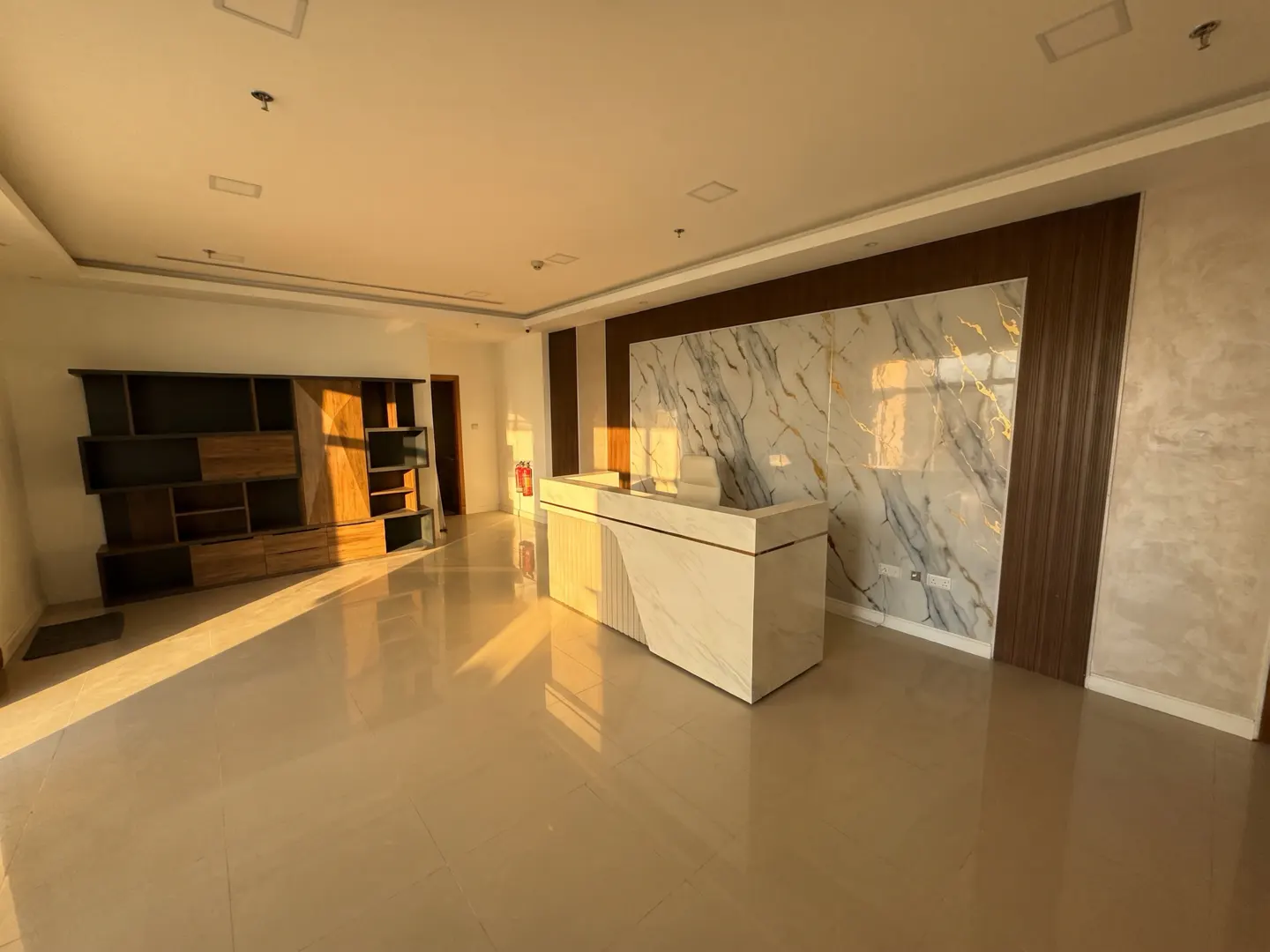 An office space with a marble reception desk, a wooden bookshelf, and beige tile flooring.