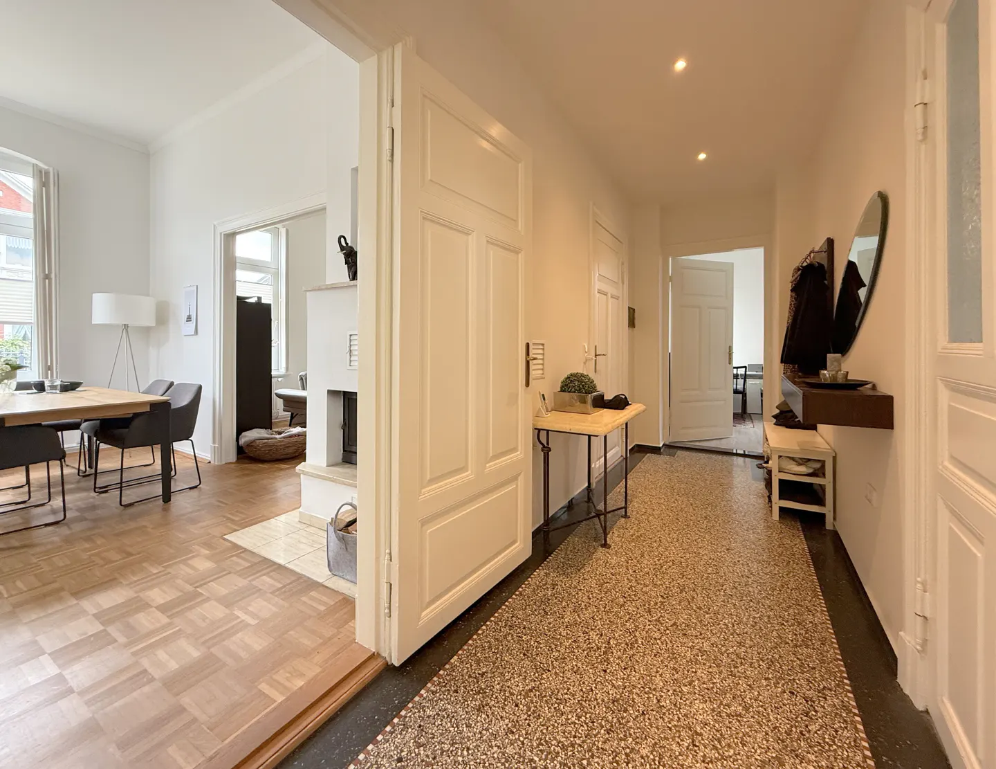 Bright hallway with terrazzo flooring leading to a dining room with parquet floors, white walls, and classic white doors.