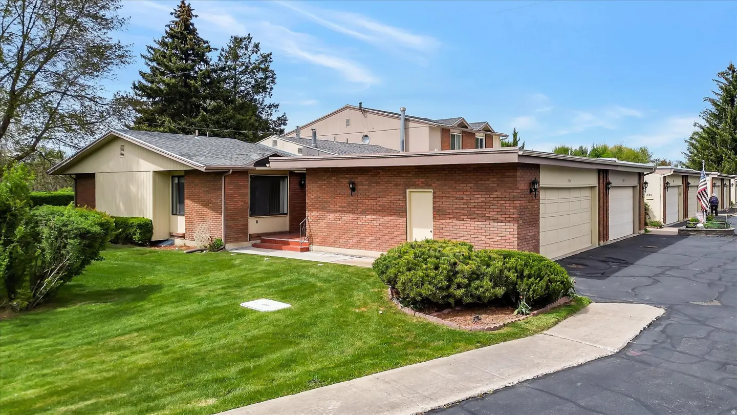 Exterior view of a single-story brick home with a green lawn and a row of garages under a blue sky.