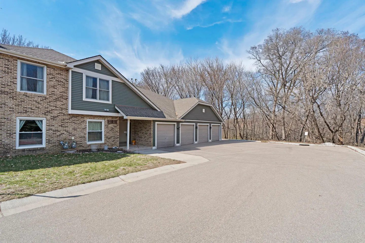 Exterior view of a two-story brick and green siding townhouse with four garage doors and a large parking area.