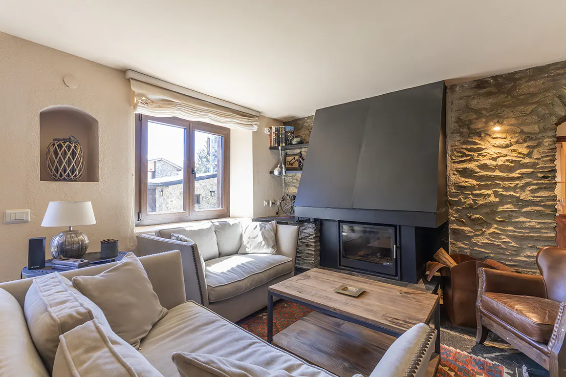 Living room with stone fireplace, beige sofas, and wooden coffee table. A window with a view is on the left.