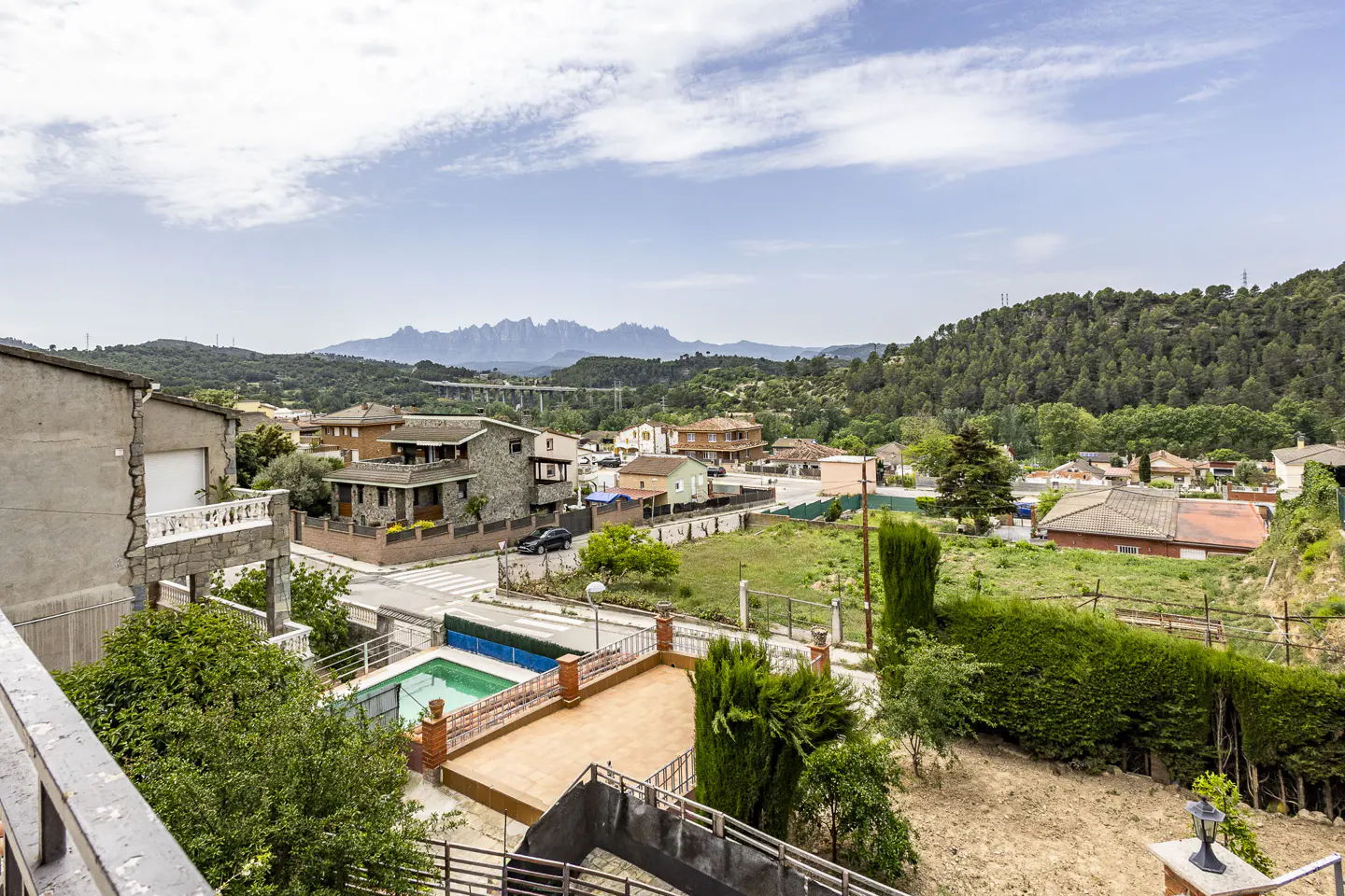 View of a residential area with houses, a pool, and mountains in the background under a cloudy sky.