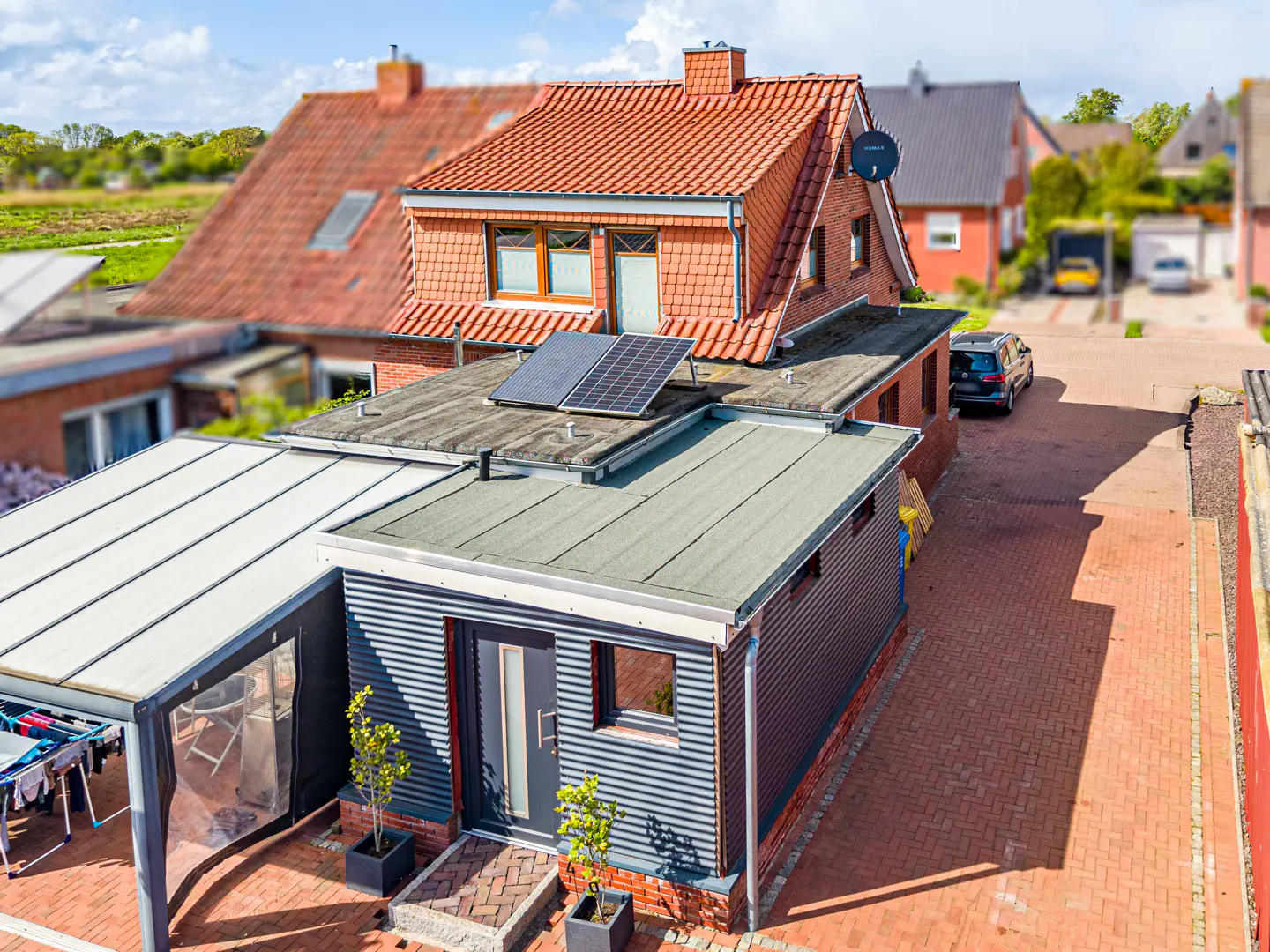 Aerial view of a house with a red tile roof, solar panels, and a corrugated metal extension with a gray door.