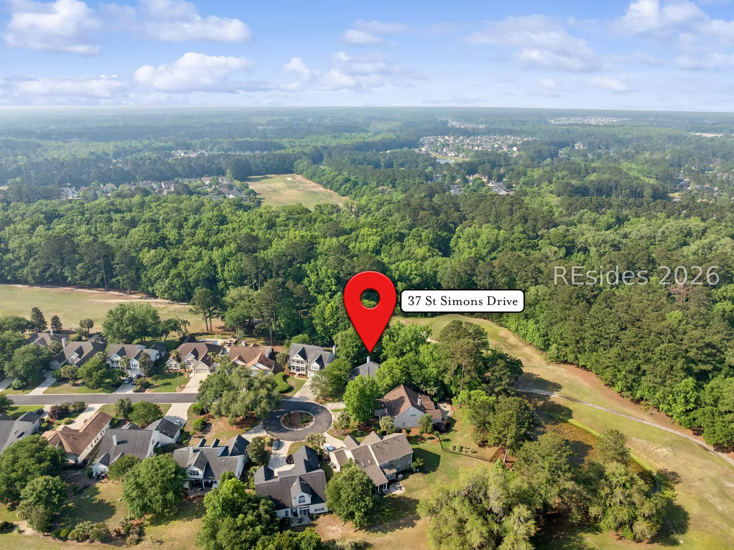 Aerial view of a neighborhood with a red map pin on 37 St Simons Drive, surrounded by green trees and a golf course.