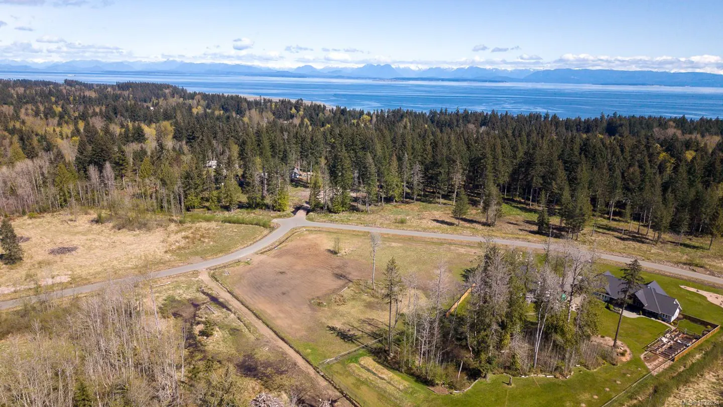 Aerial view of a property with a house, trees, and a view of the ocean and mountains in the background.
