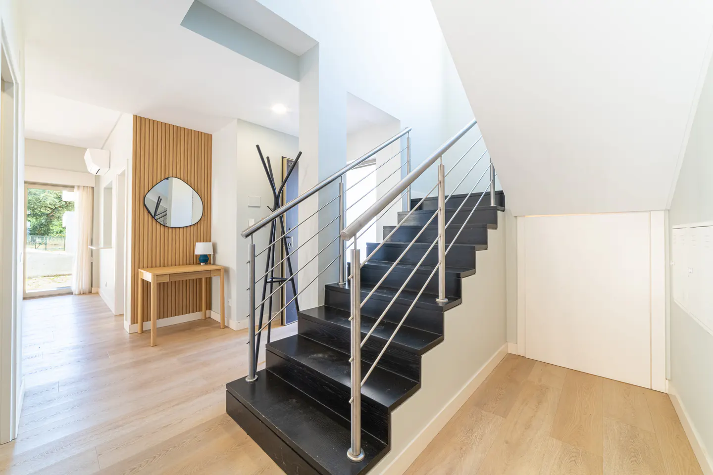 Modern entryway with black wooden stairs, metal railings, a wood-slat accent wall, a console table, and a mirror.