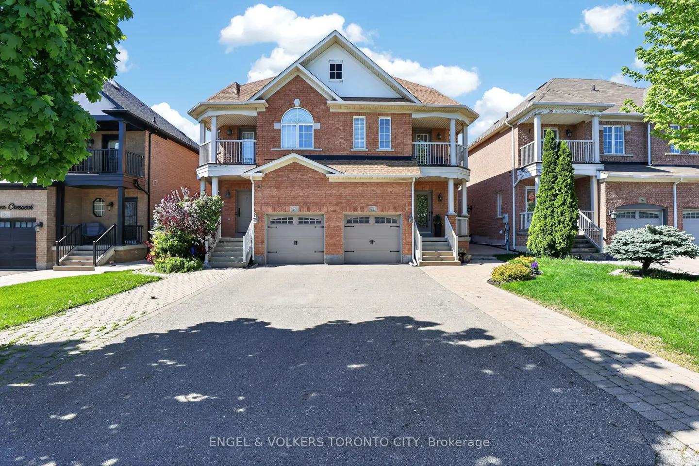 Two-story red brick duplex with two-car garages and small balconies on a sunny day.