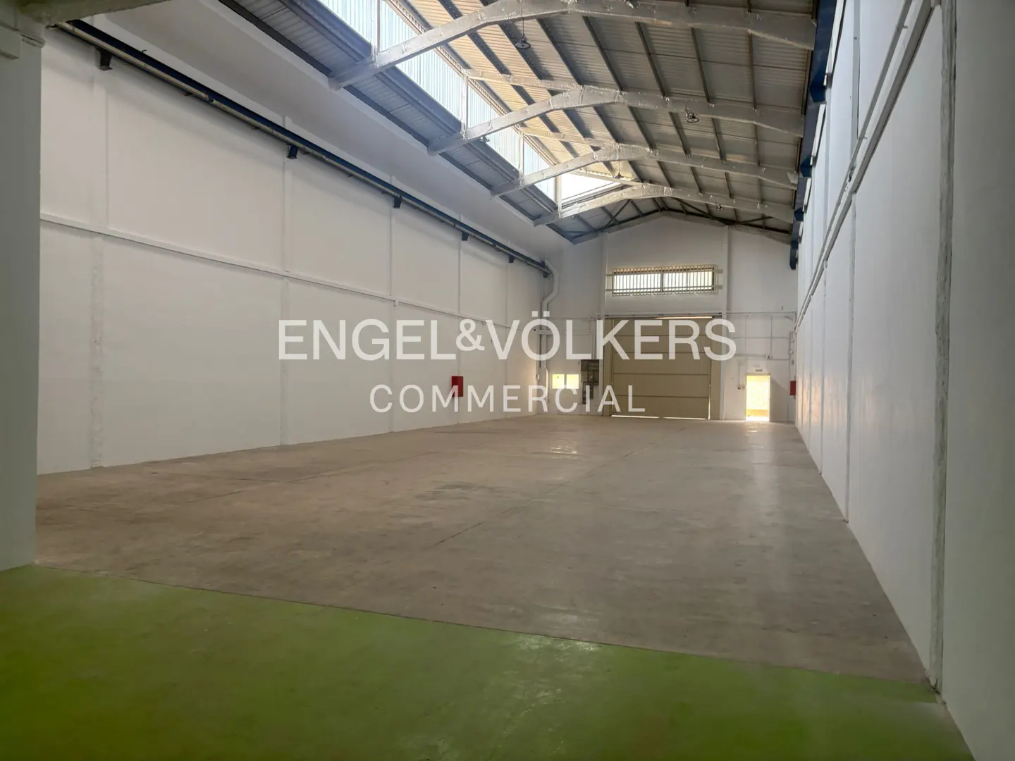 Empty, spacious industrial warehouse with white walls, concrete floors, and a high vaulted ceiling with skylights.