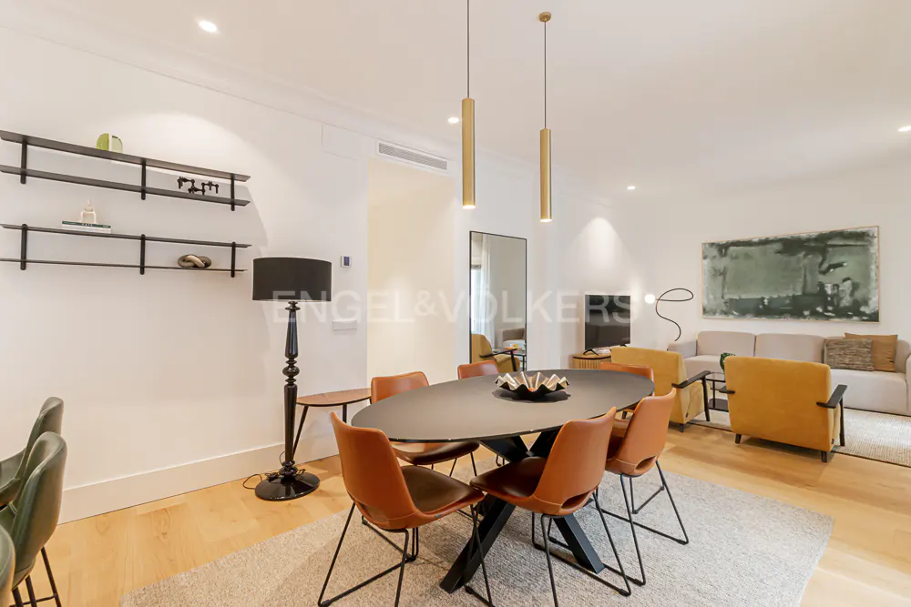 A modern living and dining area with a black oval table, orange chairs, and a beige sofa.