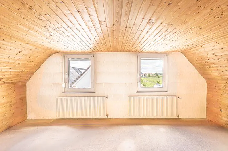 Attic room with wood paneled ceiling, white walls, two windows, and radiators.
