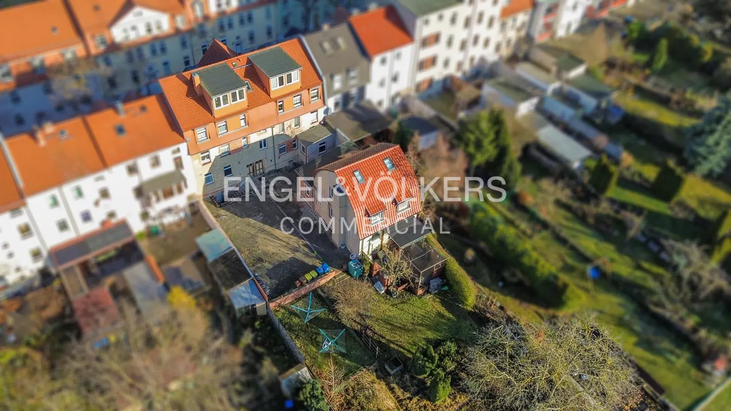 Aerial view of a multi-story building with an orange roof, surrounded by greenery and other buildings. "Engel & Völkers Commercial" is overlaid.