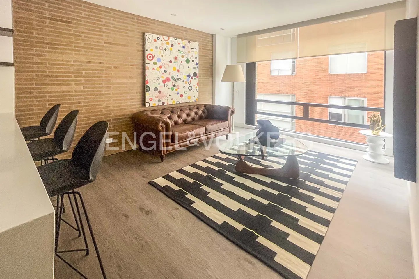 Living room with brick wall, brown leather sofa, black and white rug, and large window.