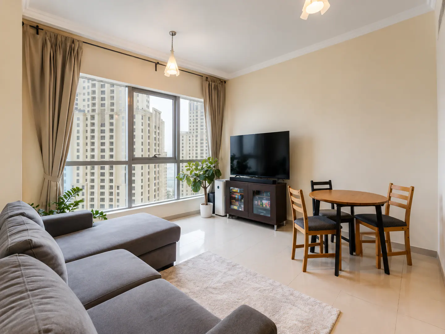 Living room with gray sectional sofa, round wood table with chairs, and a large window with city view.