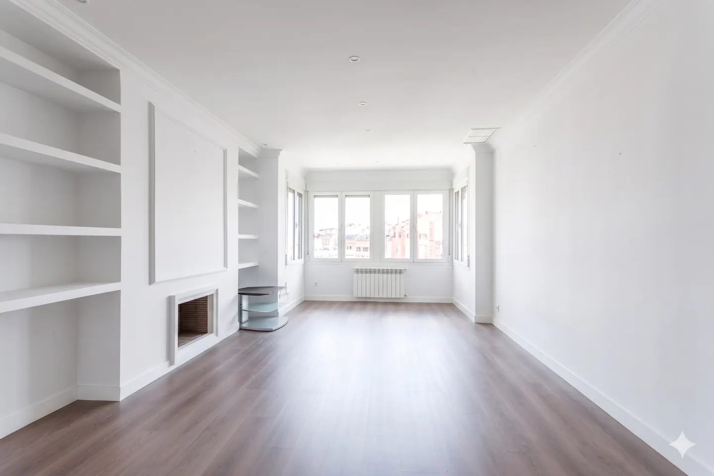 Bright, empty room with hardwood floors, white walls, and built-in shelves. Large windows offer city views.