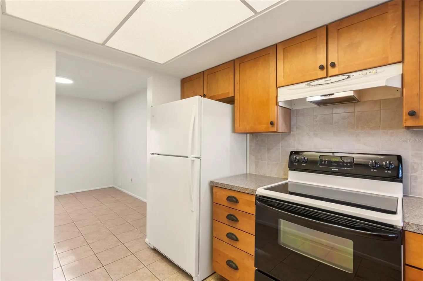 A kitchen with wood cabinets, a white refrigerator, and a black oven.