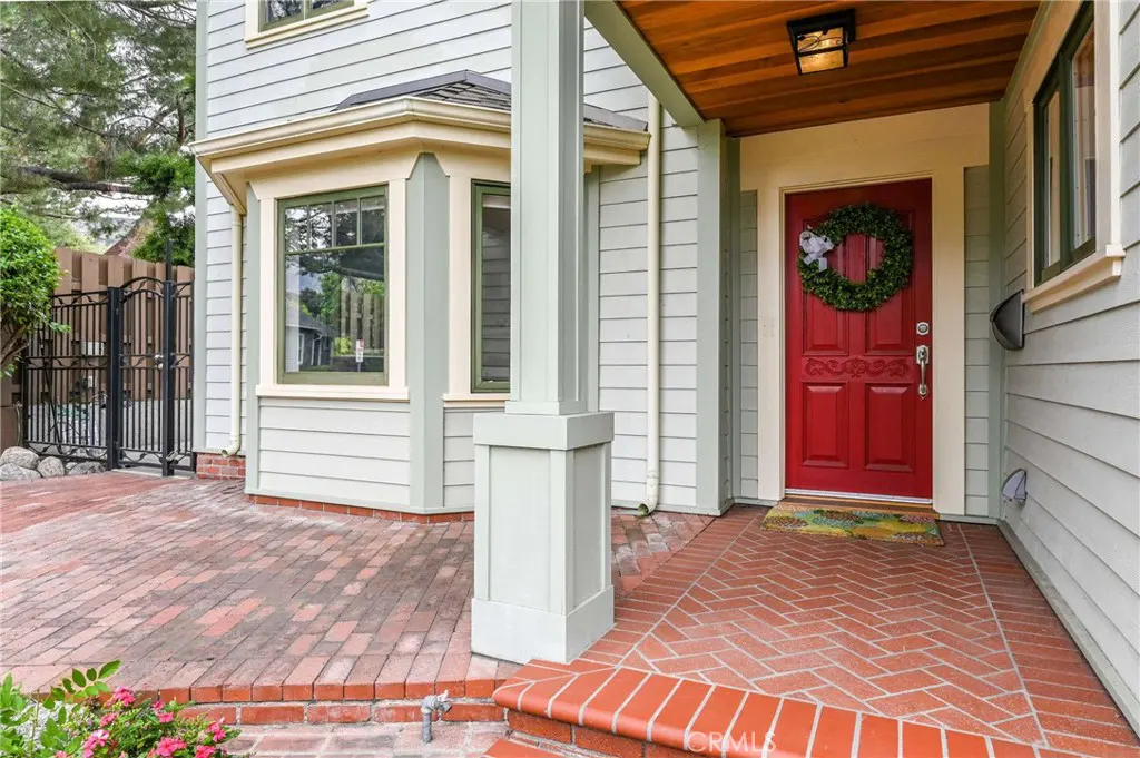 Exterior of a light green house with a red front door and brick porch. A wreath hangs on the door.