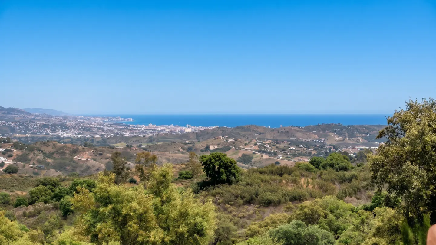 Scenic view of a coastal city from a green, hilly landscape under a clear blue sky.