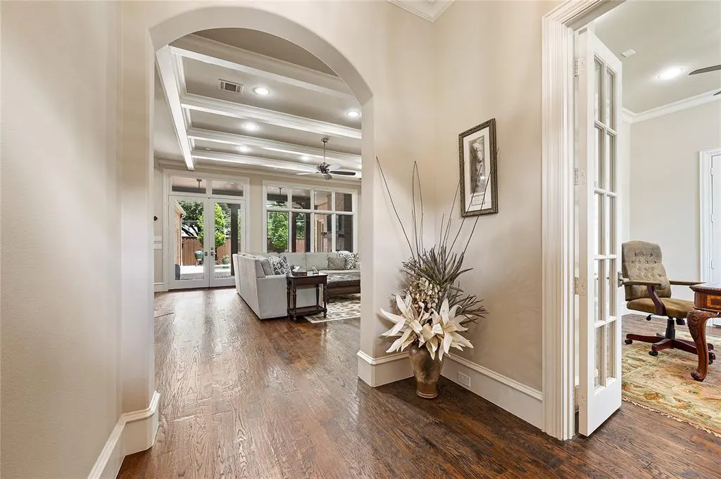 View through an arched doorway into a living room with hardwood floors, a white sectional, and a home office to the right.