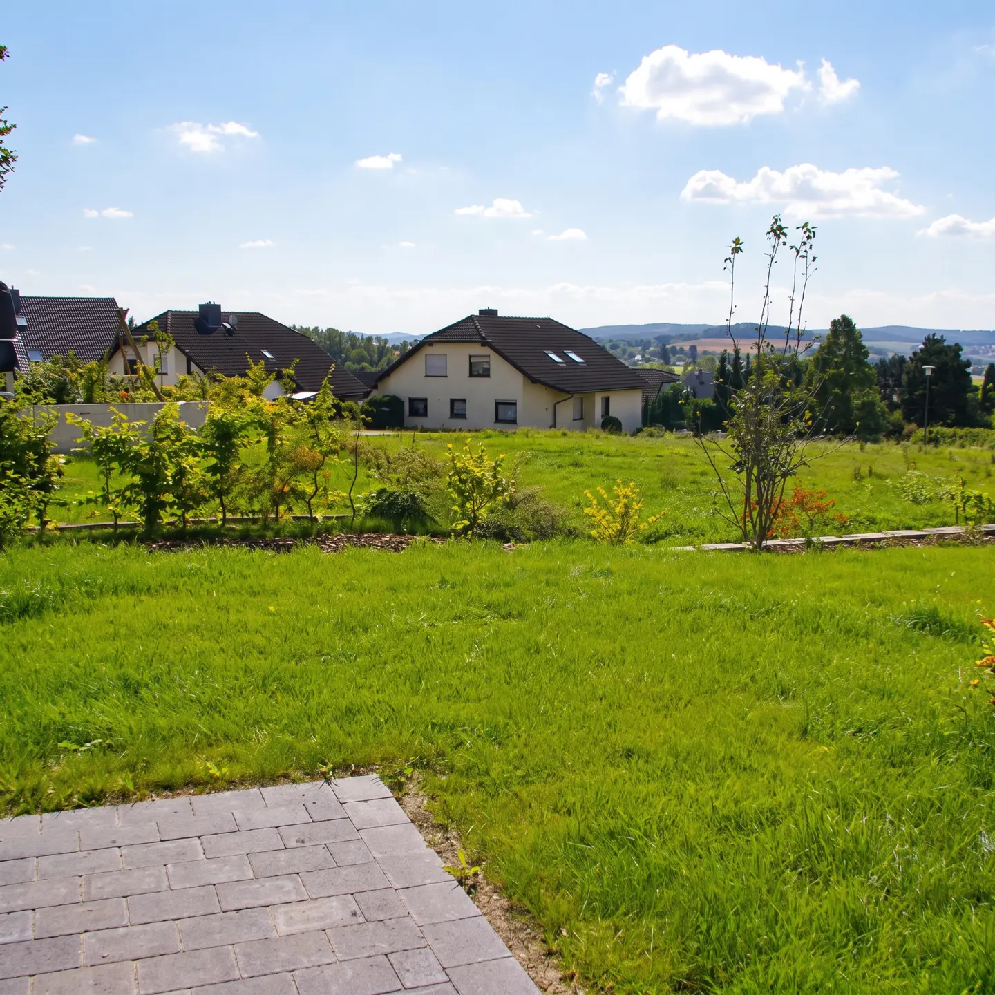 A lush green lawn leads to a house with a dark roof under a blue sky with scattered clouds.