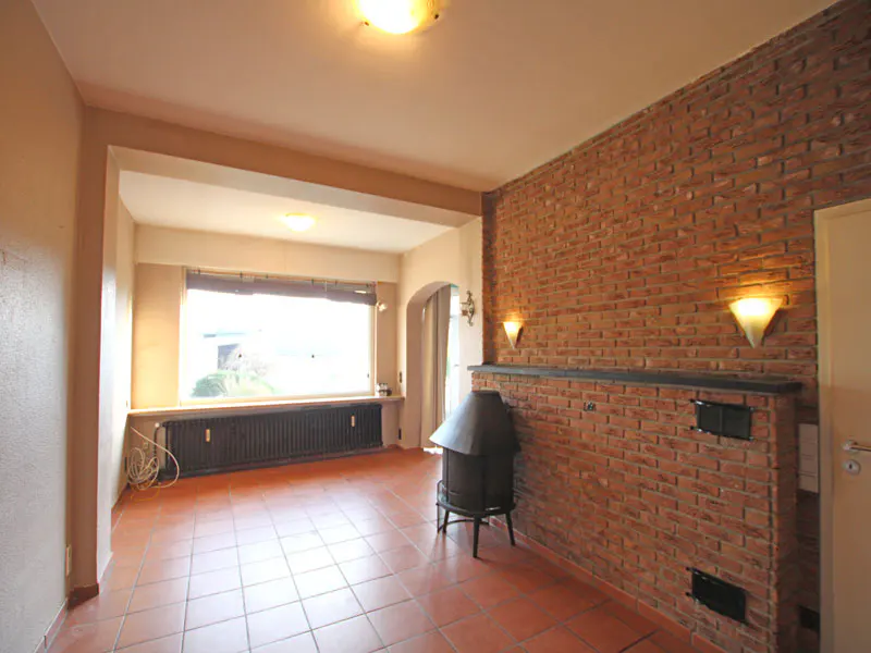 Living room with brick wall, terracotta tile floor, and black wood-burning stove. A large window is on the left.