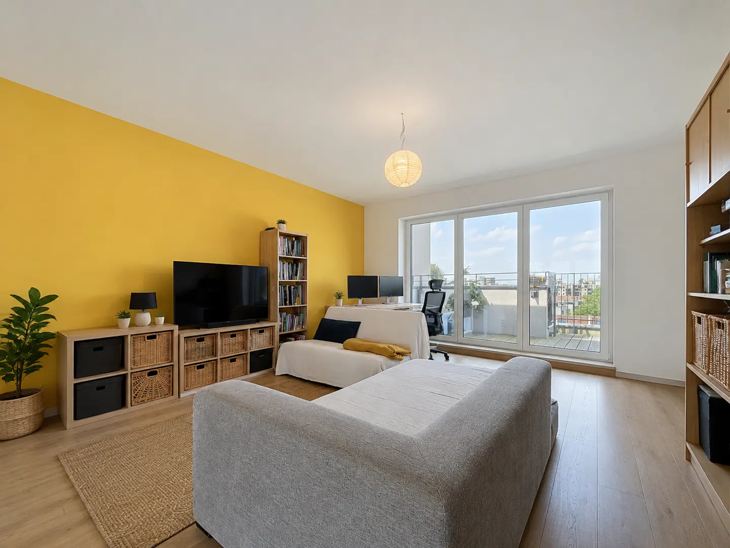Bright living room with a gray sofa, yellow accent wall, TV, and a desk by the window.