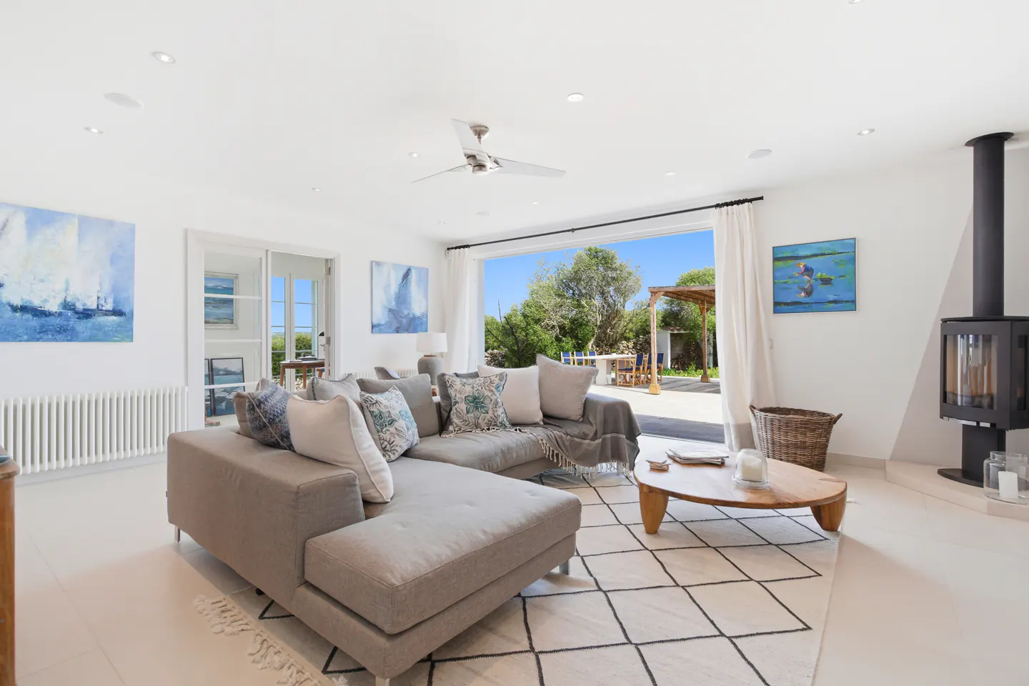 Bright living room with a gray sectional sofa, a wood coffee table, and a black fireplace. Large sliding doors open to a patio with a pergola.