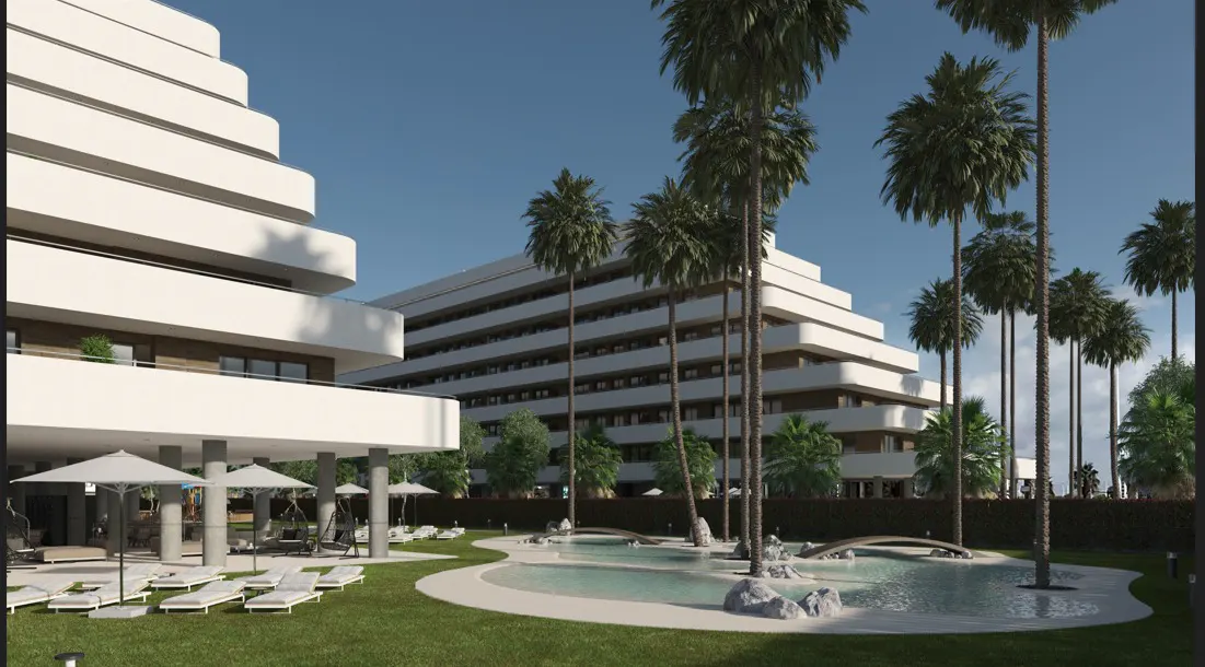 Modern white apartment buildings with tiered balconies overlook a pool and lawn area with palm trees and lounge chairs.