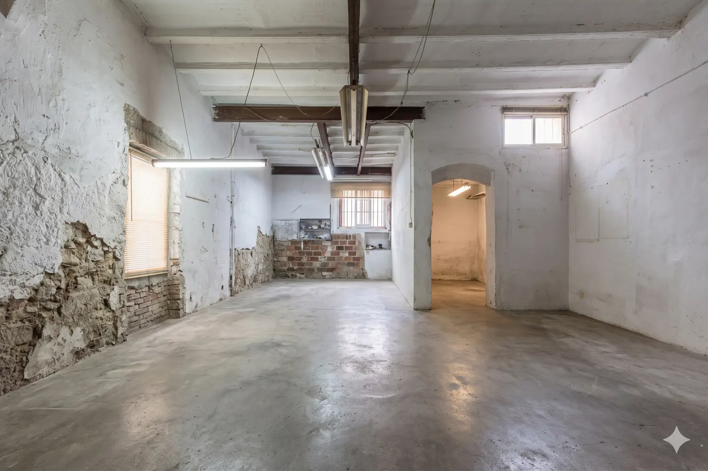Unfinished room with concrete floor, white walls with exposed brick, and fluorescent lighting.