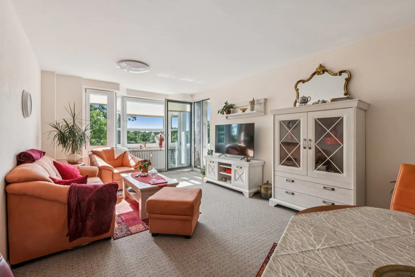 Bright living room with orange sofa, matching armchair and ottoman, white media console, and a large white display cabinet.
