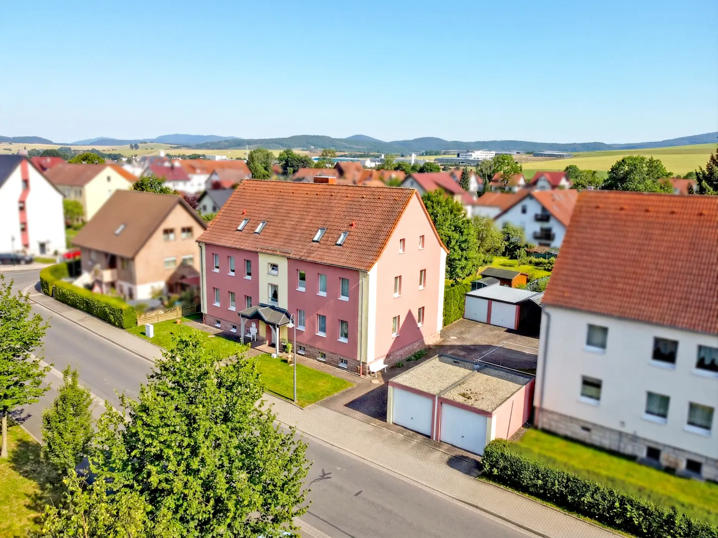 A pink, three-story apartment building with a red tile roof and white trim, sits in a residential neighborhood on a sunny day.