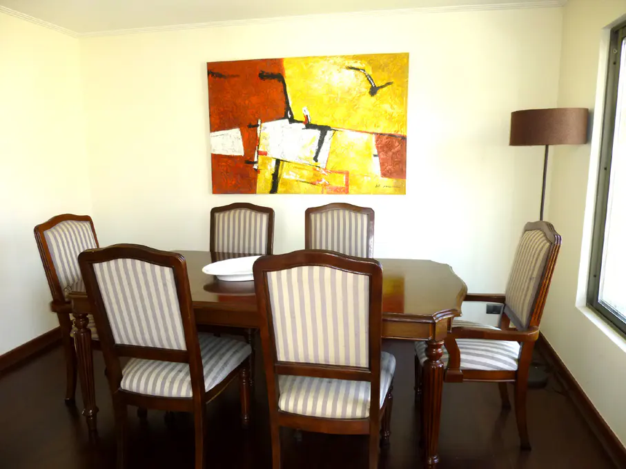 Dining room with a dark wood table and six striped chairs. An abstract painting hangs above, with a floor lamp to the right.