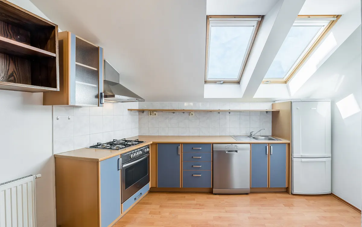 A bright kitchen with blue cabinets, stainless steel appliances, and two skylights.