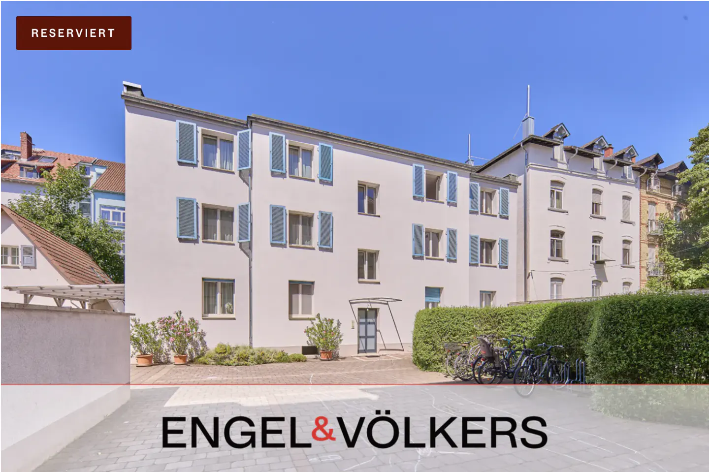 Exterior of a white apartment building with blue shutters under a clear blue sky. "Reserviert" banner in the upper left corner. Engel & Völkers logo at the bottom.