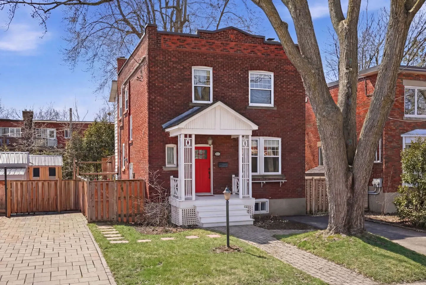 Two-story red brick house with a white porch and a bright red front door. A brick walkway leads to the house.