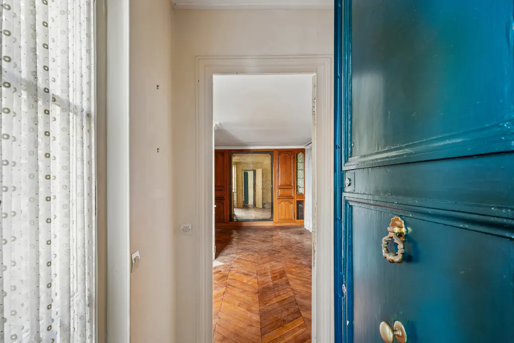 A view through an open blue door into a room with herringbone wood floors and wood paneled walls.