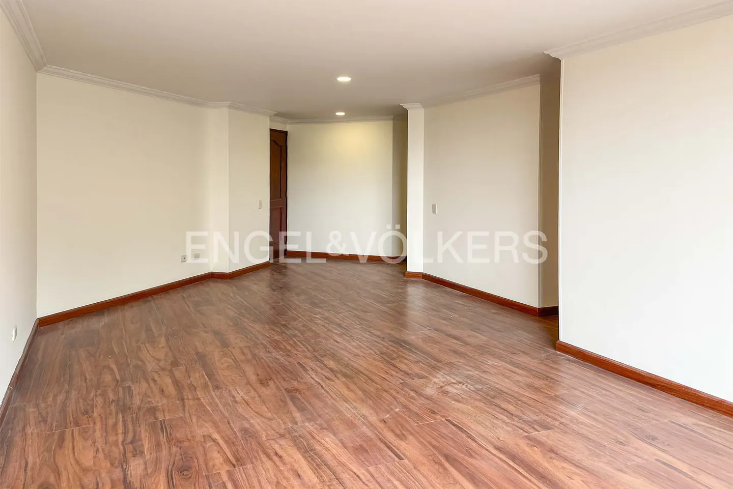 Empty room with wood floors, cream walls, and white trim. A doorway leads to another room. Engel & Völkers logo is visible.