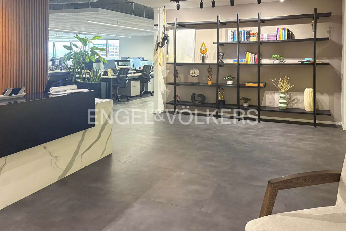 Office interior with a black reception desk, marble accents, and an open workspace with desks and chairs. A black bookshelf displays decorative items.