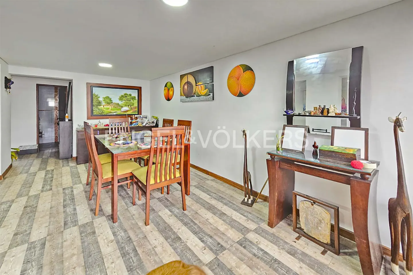 A dining room with a wooden table and chairs, art on the walls, and a wooden console table.