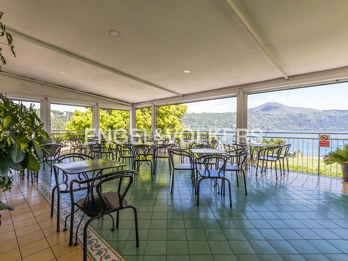 Outdoor restaurant seating area with black metal chairs and tables, green tile floor, and lake view.